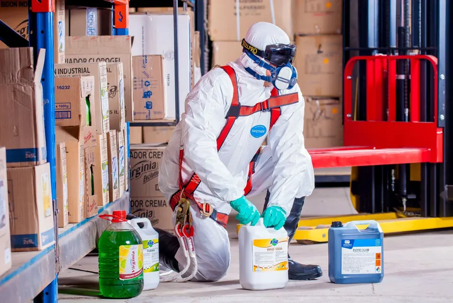 Worker in protective coveralls and respiratory equipment handling hazardous material safely