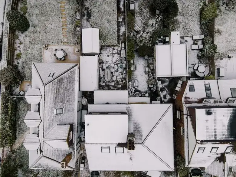 Aerial view of British terraced houses with flat-roofed rear extensions and garden outbuildings covered in snow
