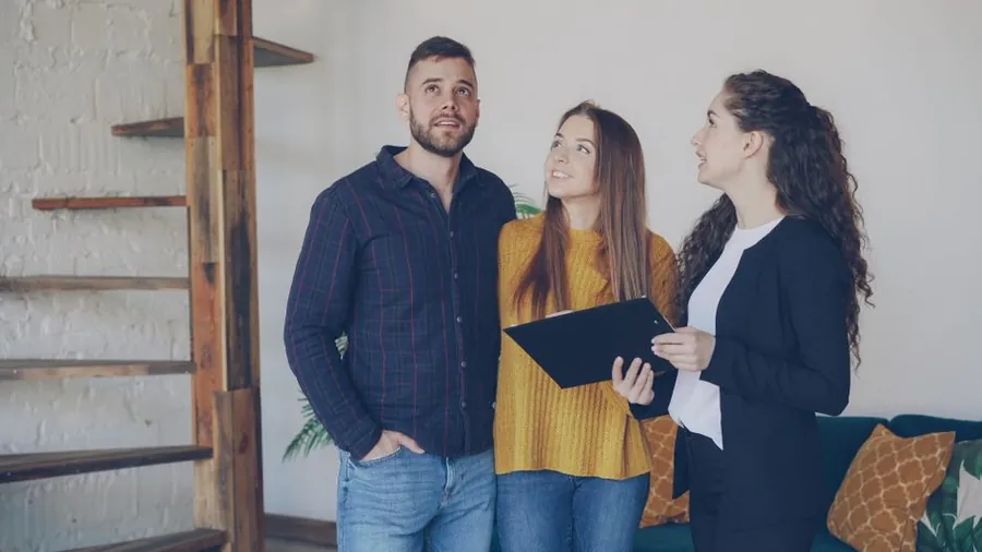 Young couple looking around a property with an estate agent holding a folder