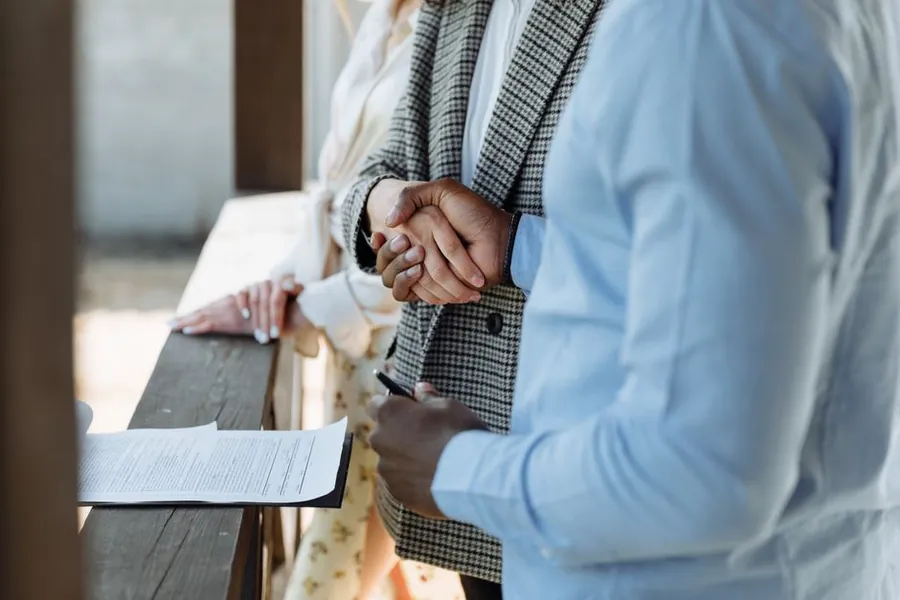 Two people shaking hands over a signed property agreement on a wooden rail