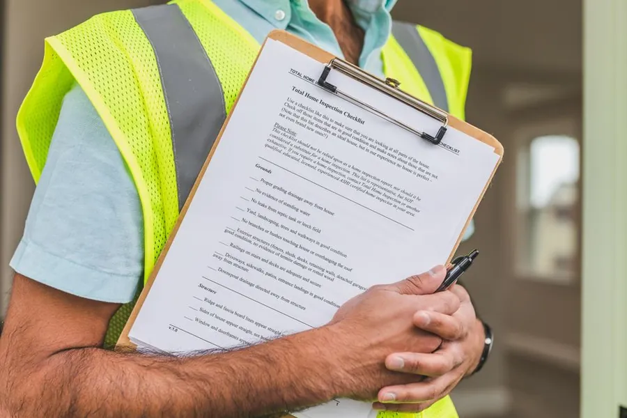 Inspector in a high-visibility vest holding a clipboard checklist and pen