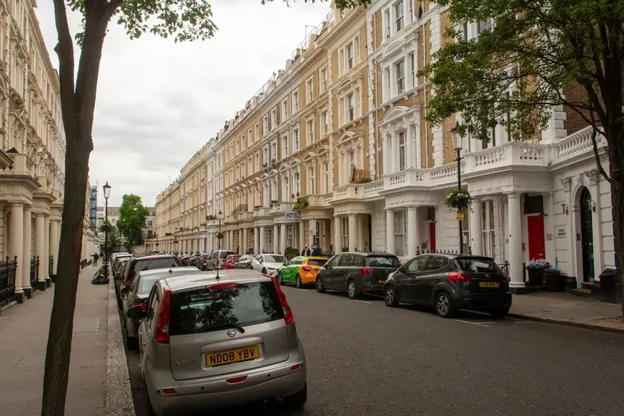 Long terrace of period townhouses on a leafy British street with cars parked outside