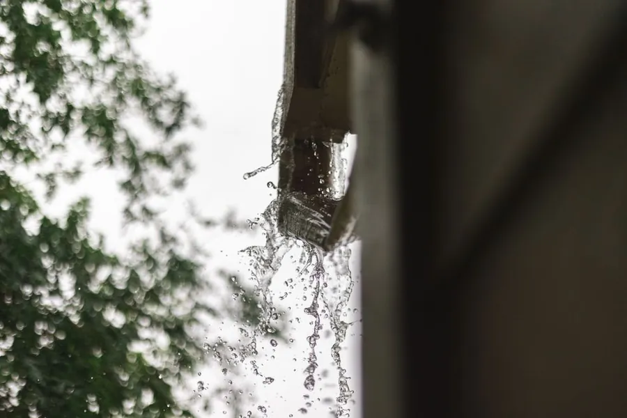 Rainwater overflowing from a roof gutter and downpipe during heavy rain