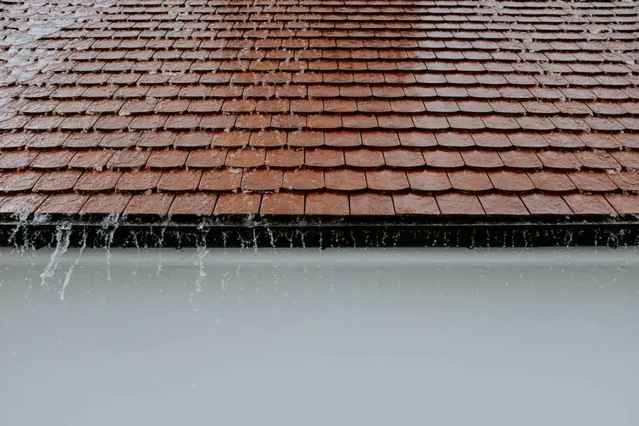 Heavy rain running off a roof edge and pouring past a gutter
