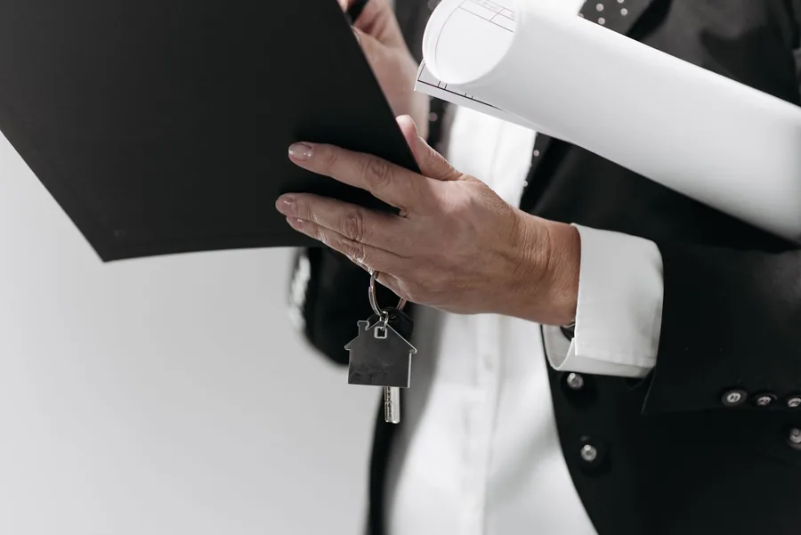 Person holding architectural plans and a house key while reviewing a property project