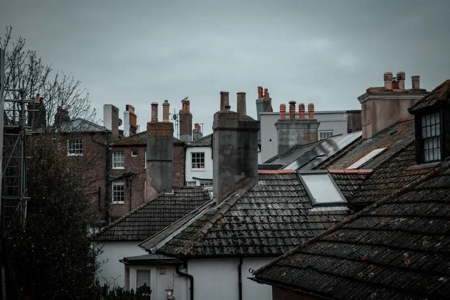 Grey rooftops and clustered chimney stacks of British houses under an overcast sky
