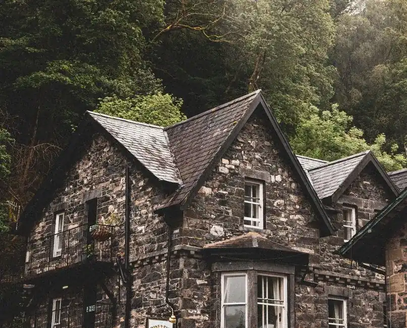 Traditional stone house with slate roofs and gables backed by mature trees