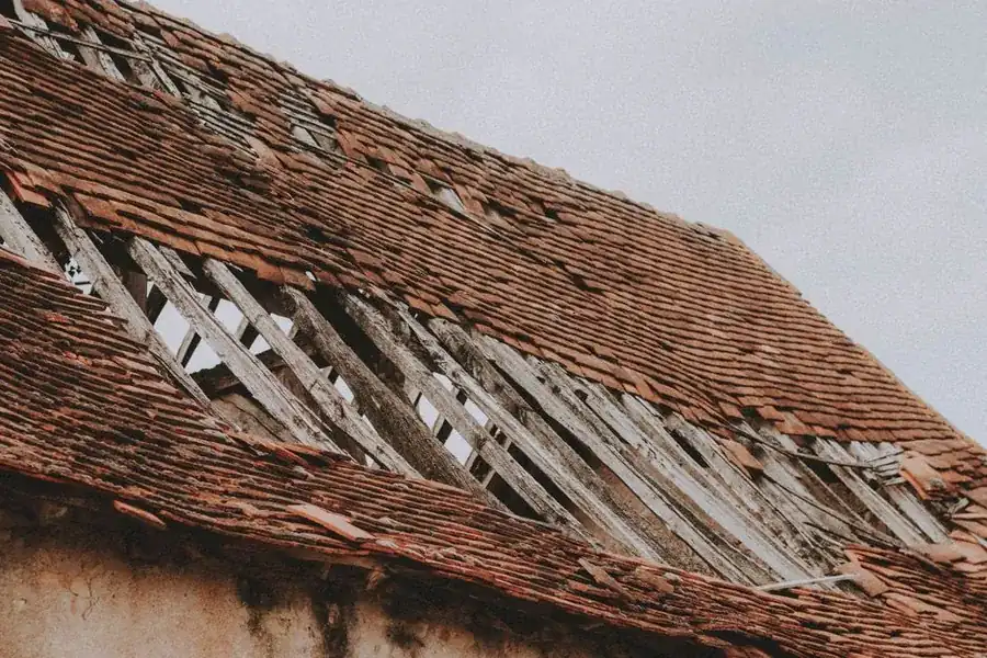 Old roof with tiles removed showing weathered timber battens and exposed structure beneath