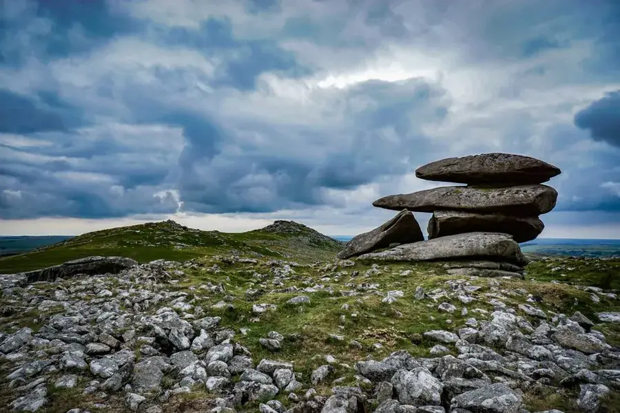 Weathered layered rock outcrop with flat stacked stone slabs on English moorland under a heavy sky
