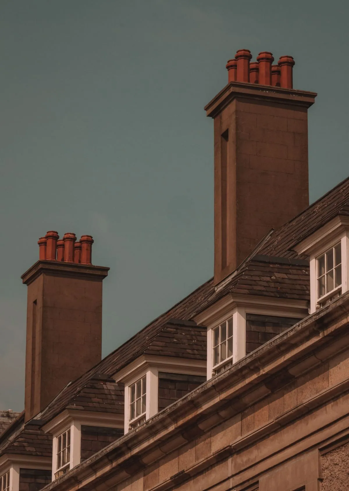 Row of brick chimney stacks on a sloped rooftop against a gray sky