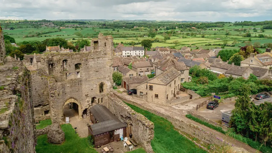 Aerial view of medieval stone castle ruins beside a village and green countryside under cloudy skies