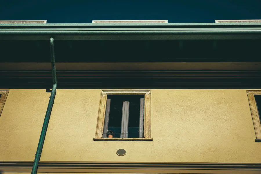 Low-angle view of a yellow building facade with a small open window and dark roofline