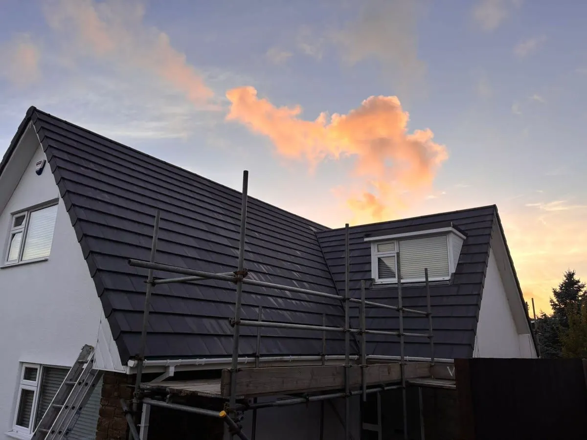 House with dark roof under construction, fronted by scaffolding at sunset