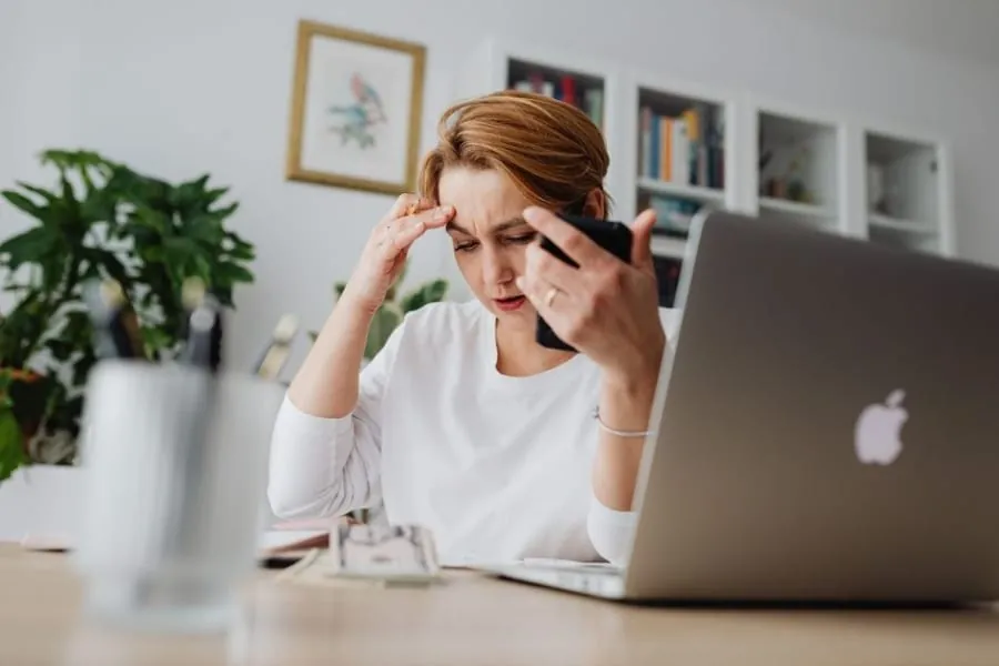 Homeowner looking concerned while reviewing contractor paperwork and phone at a desk