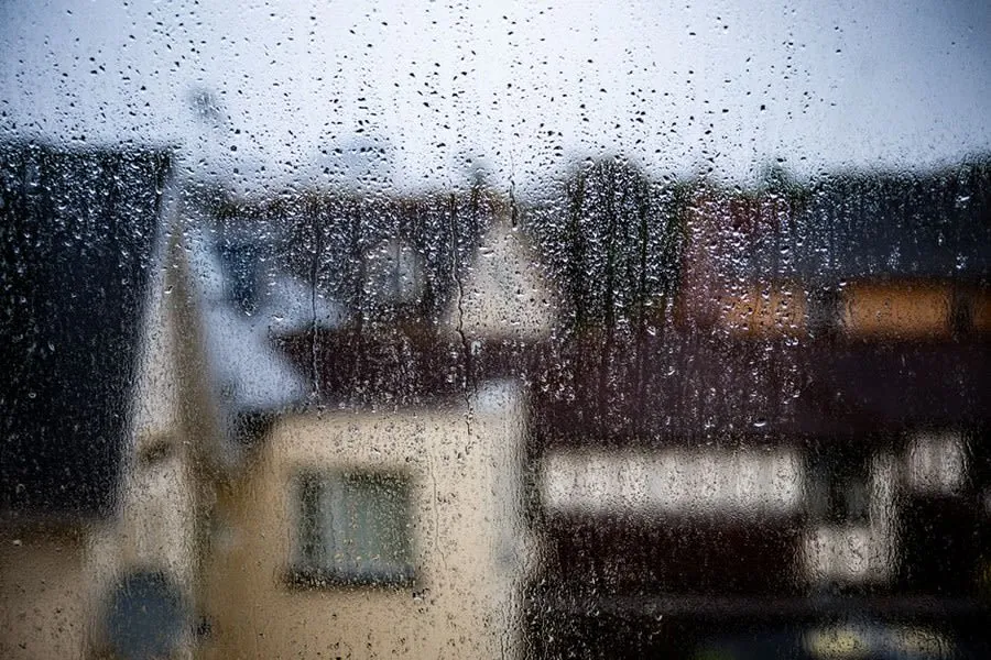 Rain running down a window overlooking rooftops on a wet winter day
