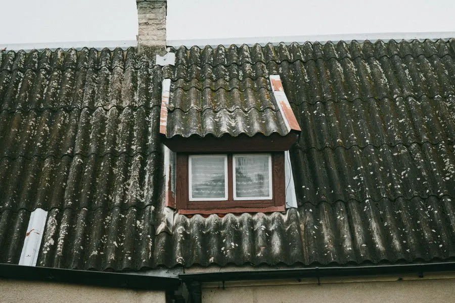Dormer window on a weathered tiled roof with a chimney in the background