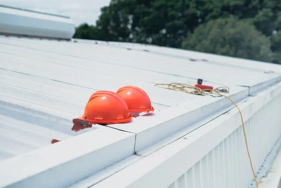 Two orange hard hats on a white rooftop beside safety gear and a rope line.