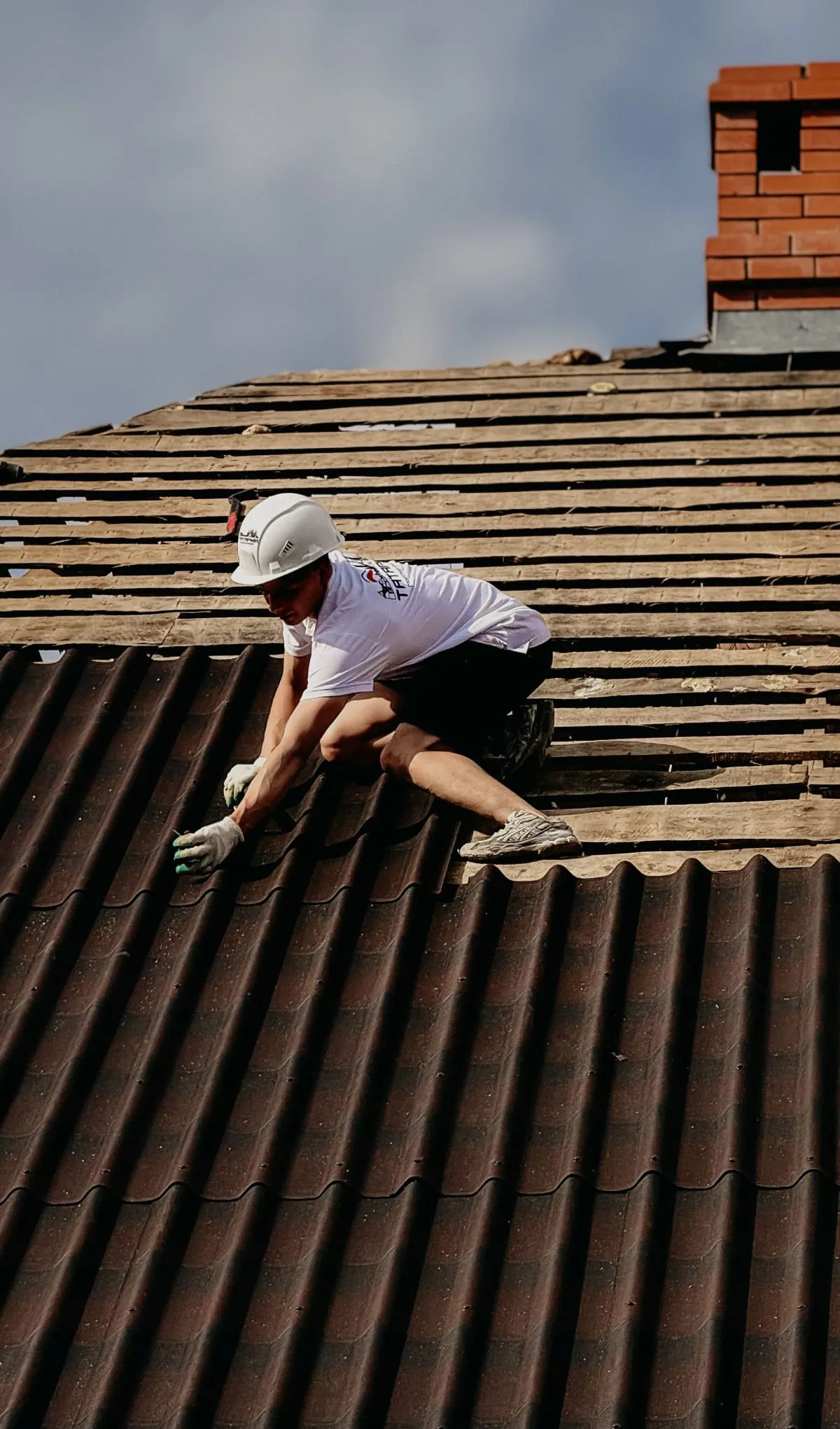 Worker on a corrugated rooftop repairing slates beside a brick chimney