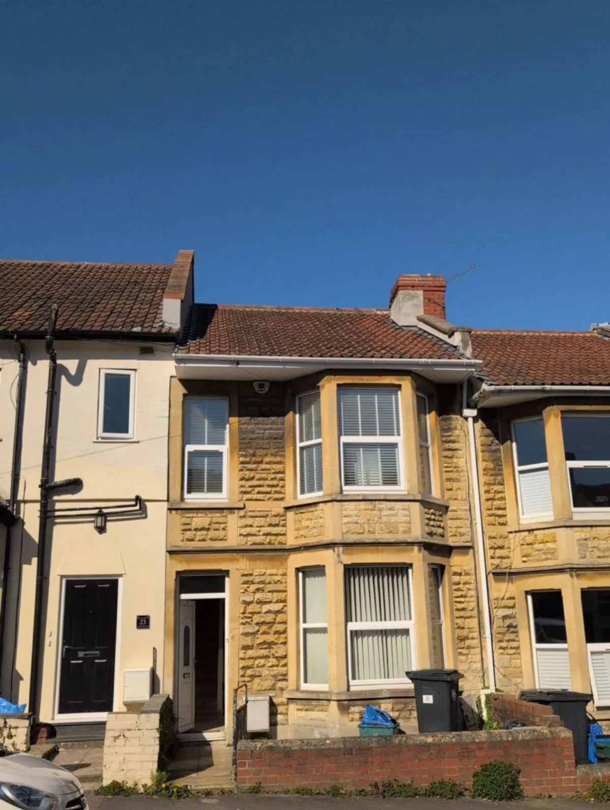Row of terraced houses with cream brick facades and red-tiled roofs under a clear blue sky