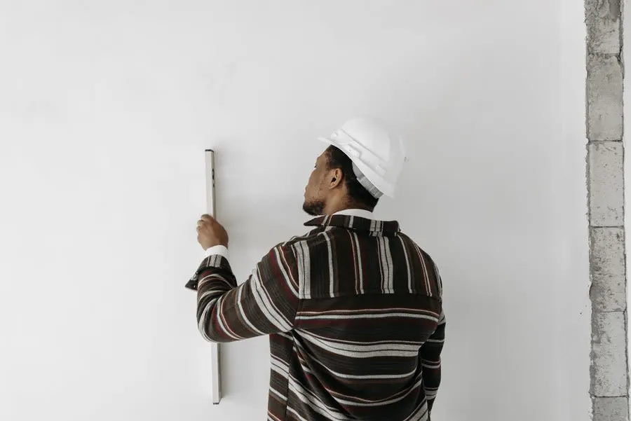 Person in a hard hat measuring a white wall with a level at a construction site.