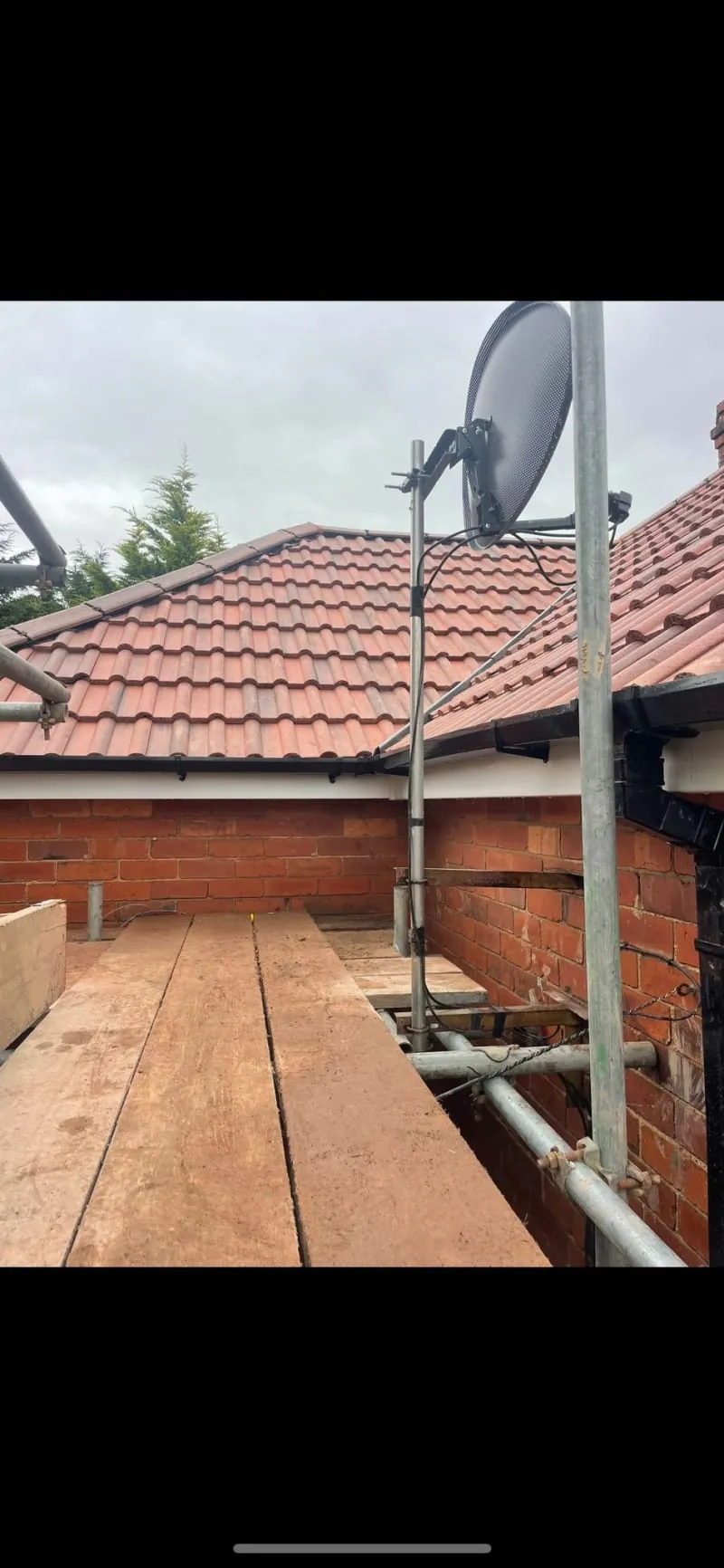 A large circular saw blade attached to metal scaffolding on the side of a brick house with a tiled roof.