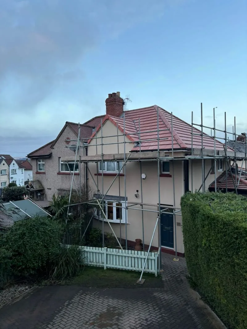 A detached house under renovation with scaffolding around the front facade and a newly tiled roof.