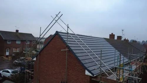 A residential house with a new dark-tiled roof and metal scaffolding structures installed on the side and front.
