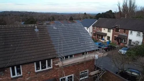 A brick residential building with a partially replaced dark roof, featuring scaffolding during a renovation process.